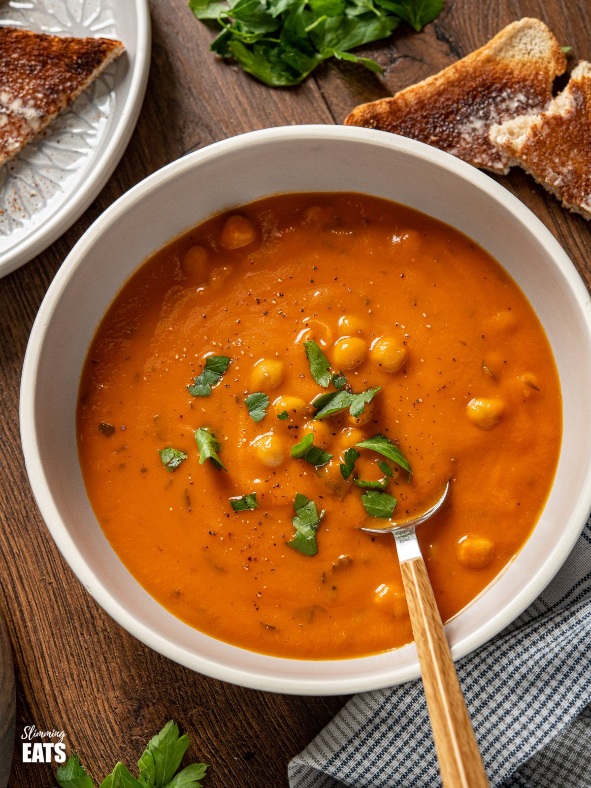 chickpeas and tomato soup in grey bowl with spoon and scattered parsley