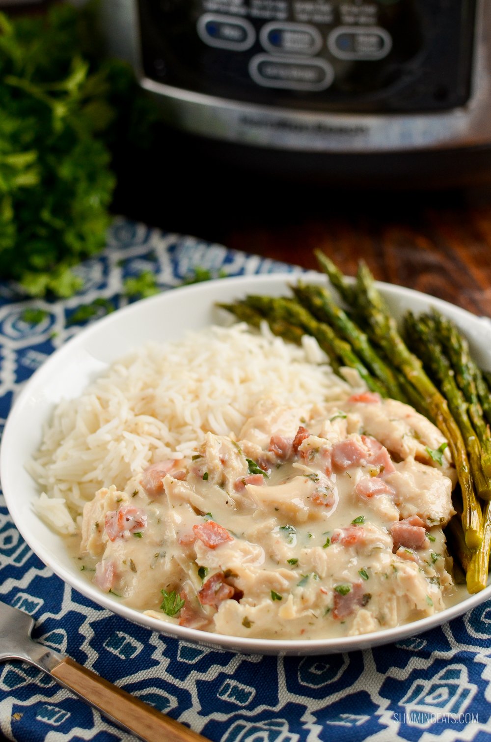 Healthier Slow Cooker Crack Chicken - the ultimate family-friendly creamy chicken recipe topped with the yummy smokey flavour of bacon. Oh my!! #slimming #weightwatchers #chicken #slowcooker #glutenfree #bacon #creamy white plate of slow cooker crack chicken with rice and asparagus on blue patterned placemat