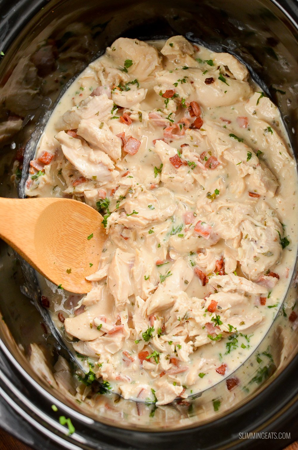 Healthier Slow Cooker Crack Chicken - the ultimate family-friendly creamy chicken recipe topped with the yummy smokey flavour of bacon. Oh my!! #slimming #weightwatchers #chicken #slowcooker #glutenfree #bacon #creamy healthier crack chicken in slow cooker with wooden spoon