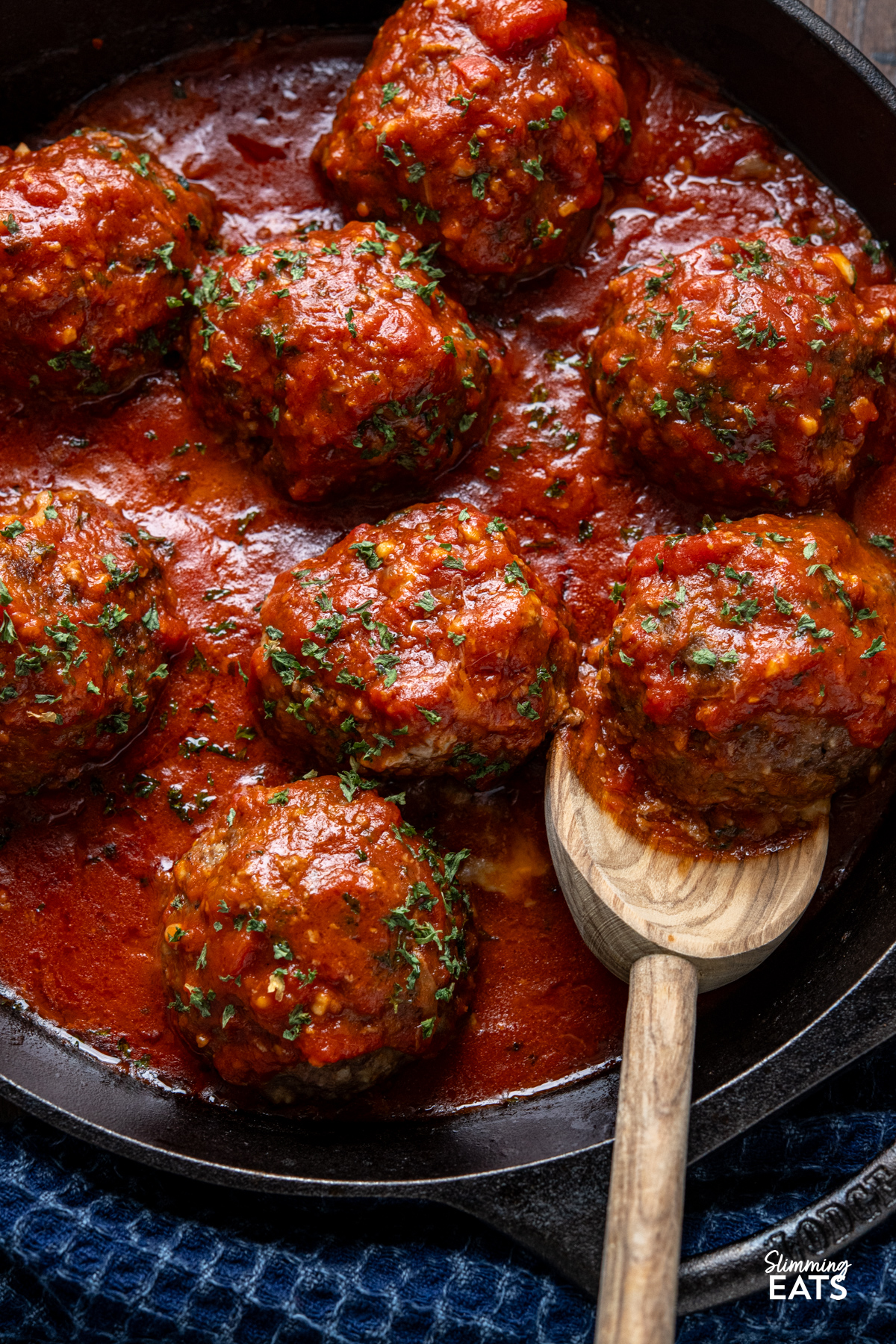 close up of Mega Stuffed Meatballs with Tomato Sauce in a black cast iron skillet with wooden spoon
