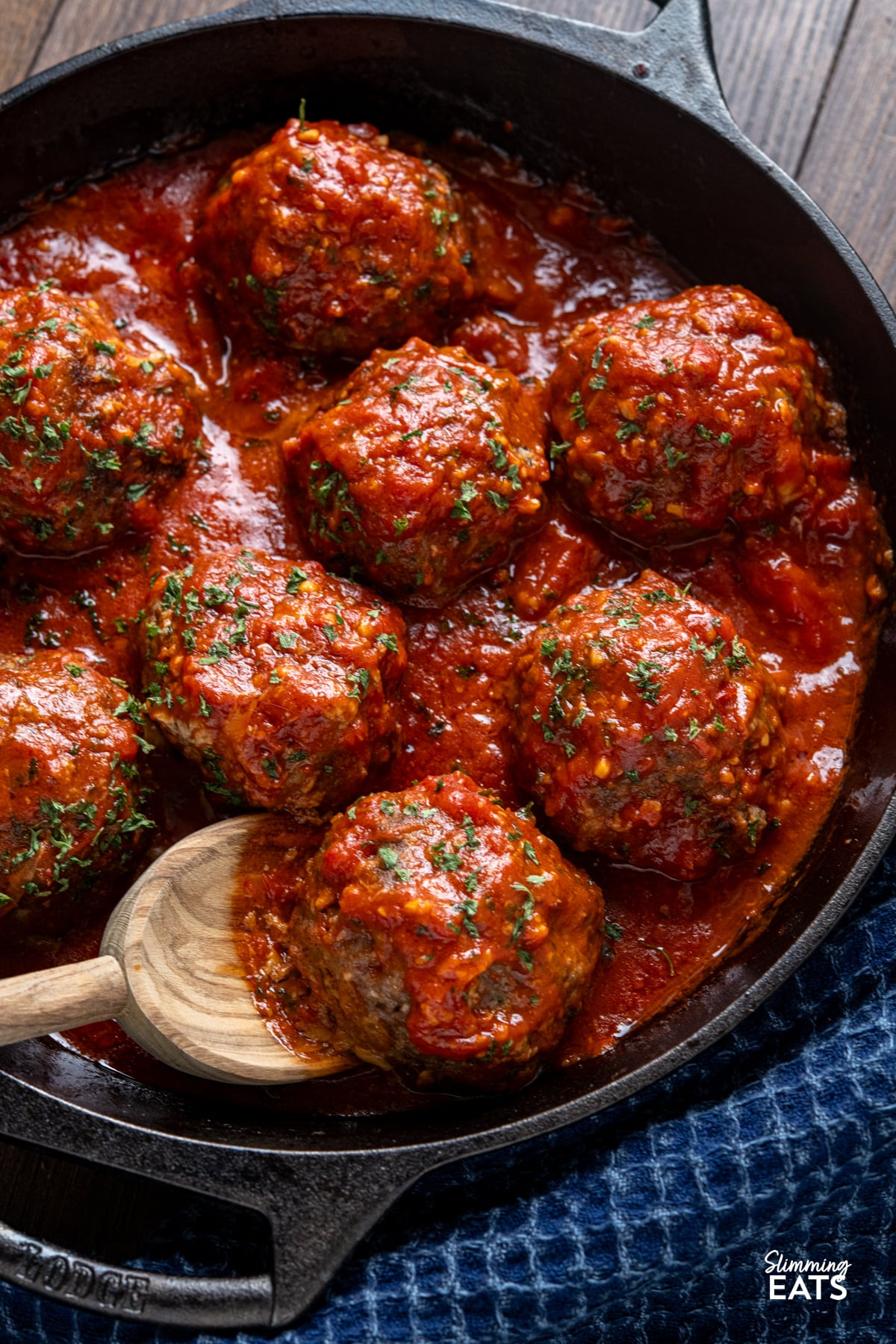 close up of Mega Stuffed Meatballs with Tomato Sauce in a black double handled cast iron skillet with wooden spoon. 