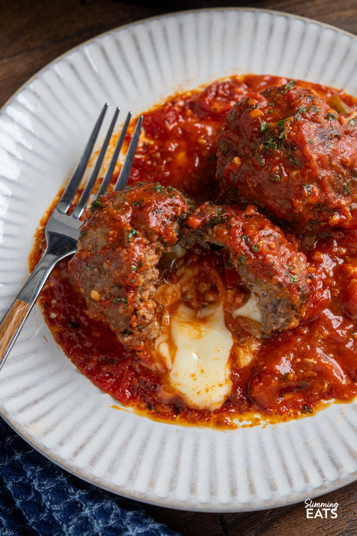 close up of Mega Stuffed Meatballs with Tomato Sauce sliced open on a plate with fork, showing melted cheese oozing out.