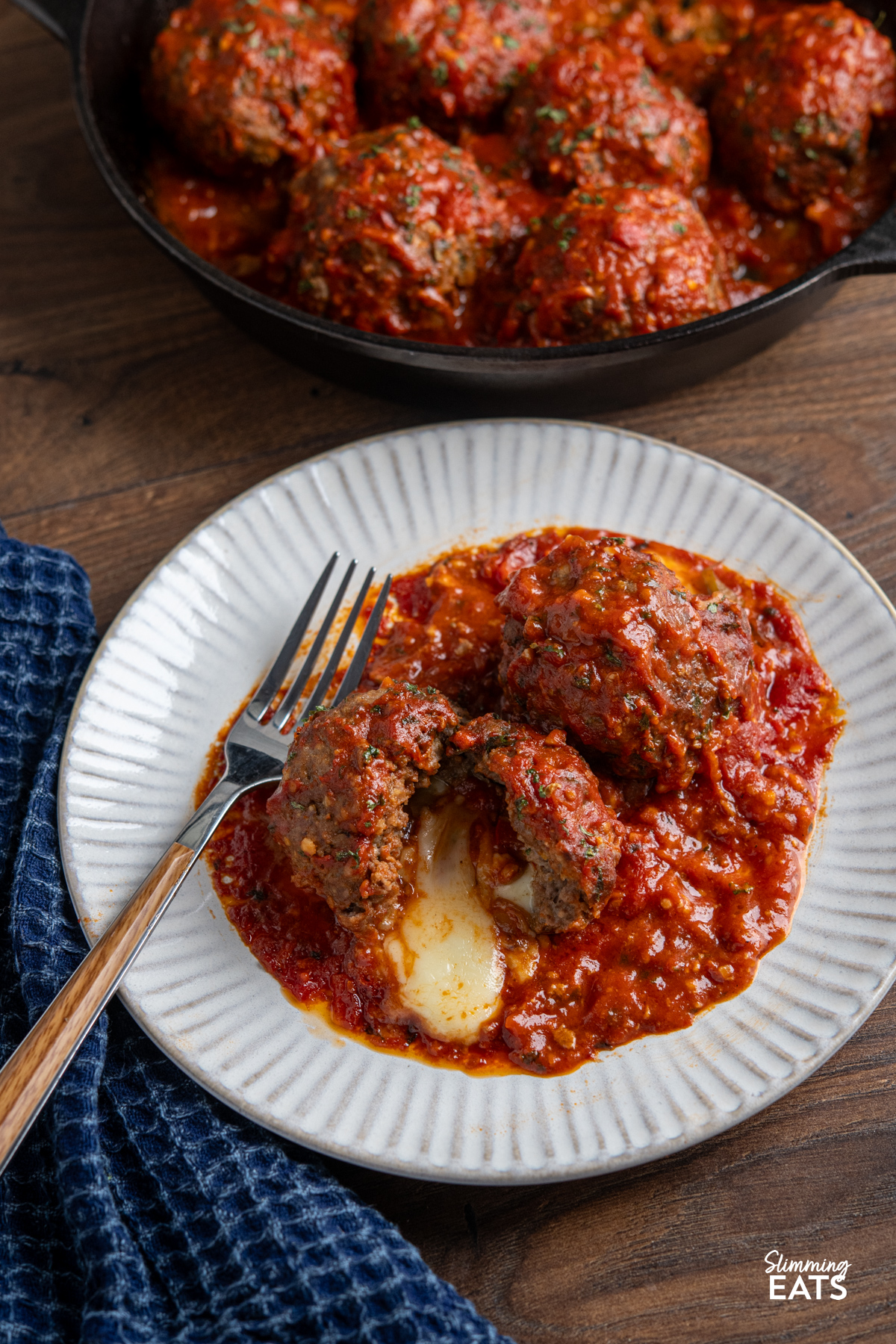 Mega Stuffed Meatballs with Tomato Sauce sliced open on a plate with fork, showing melted cheese oozing out.