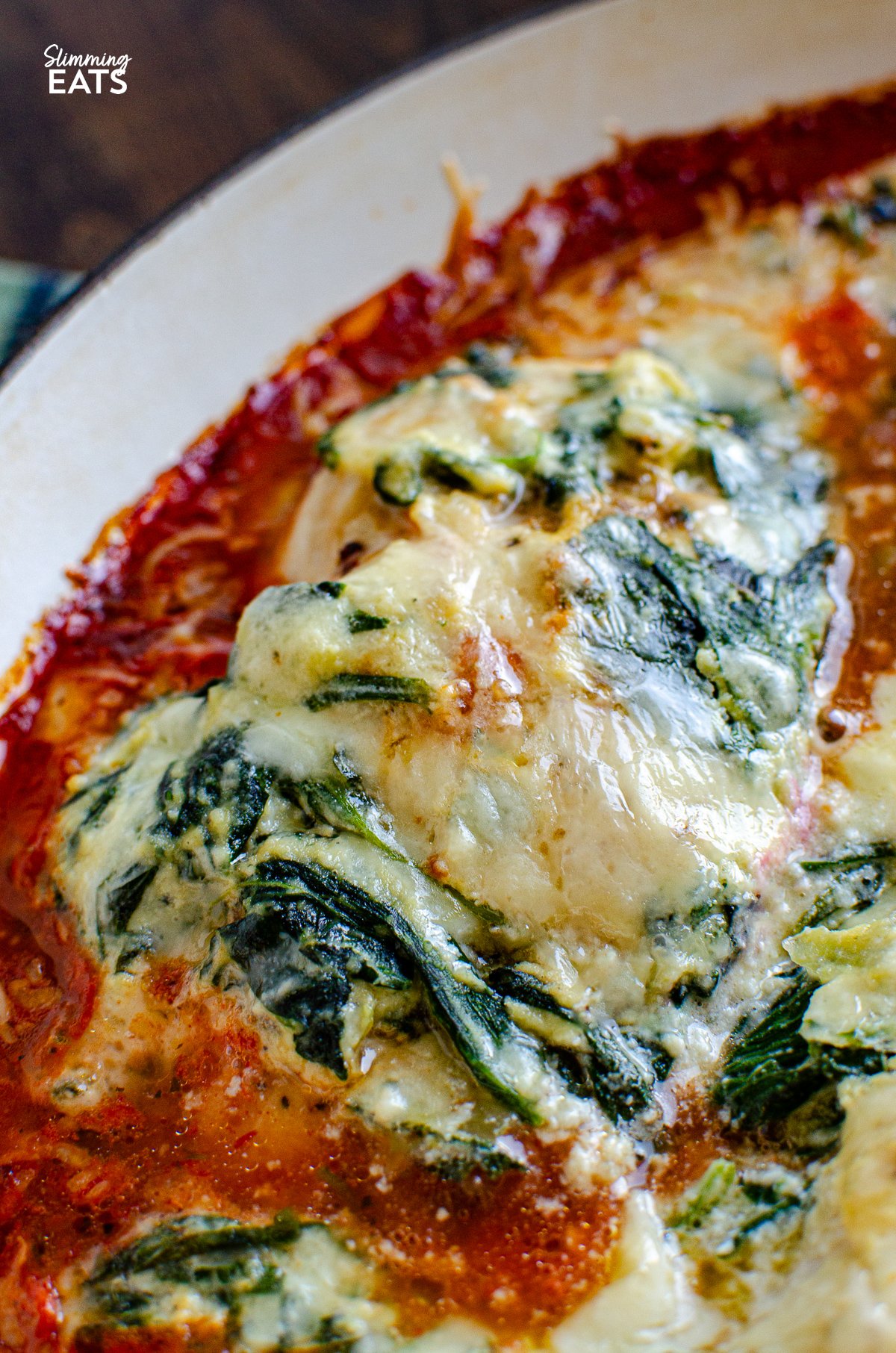This Ricotta Spinach Topped Chicken is a family-friendly recipe - tender chicken breasts resting atop a luscious tomato sauce, crowned with a generous dollop of creamy, garlicky ricotta cheese, and spinach. close up of Ricotta Spinach Topped Chicken in cast iron skillet with spatula