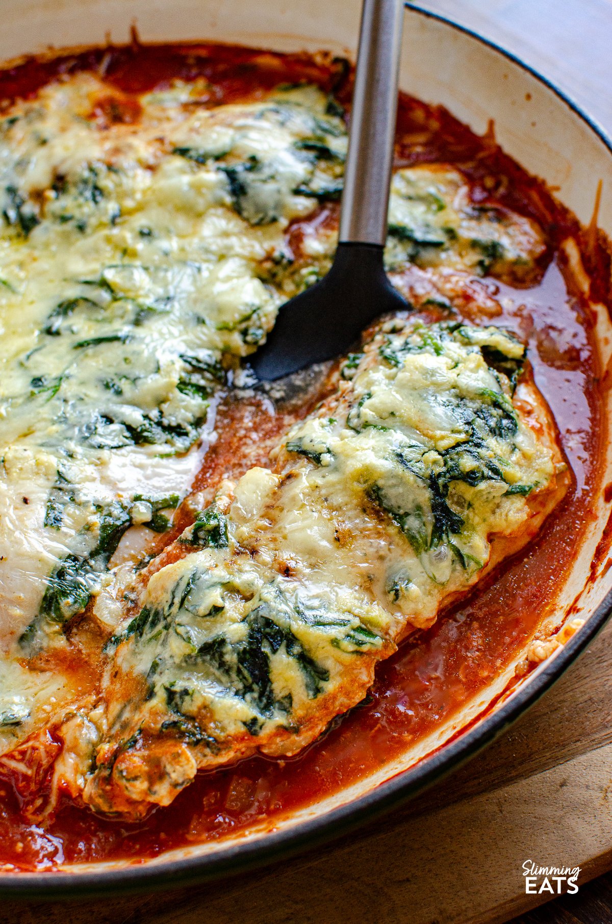 This Ricotta Spinach Topped Chicken is a family-friendly recipe - tender chicken breasts resting atop a luscious tomato sauce, crowned with a generous dollop of creamy, garlicky ricotta cheese, and spinach. Ricotta Spinach Topped Chicken in cast iron skillet with spatula