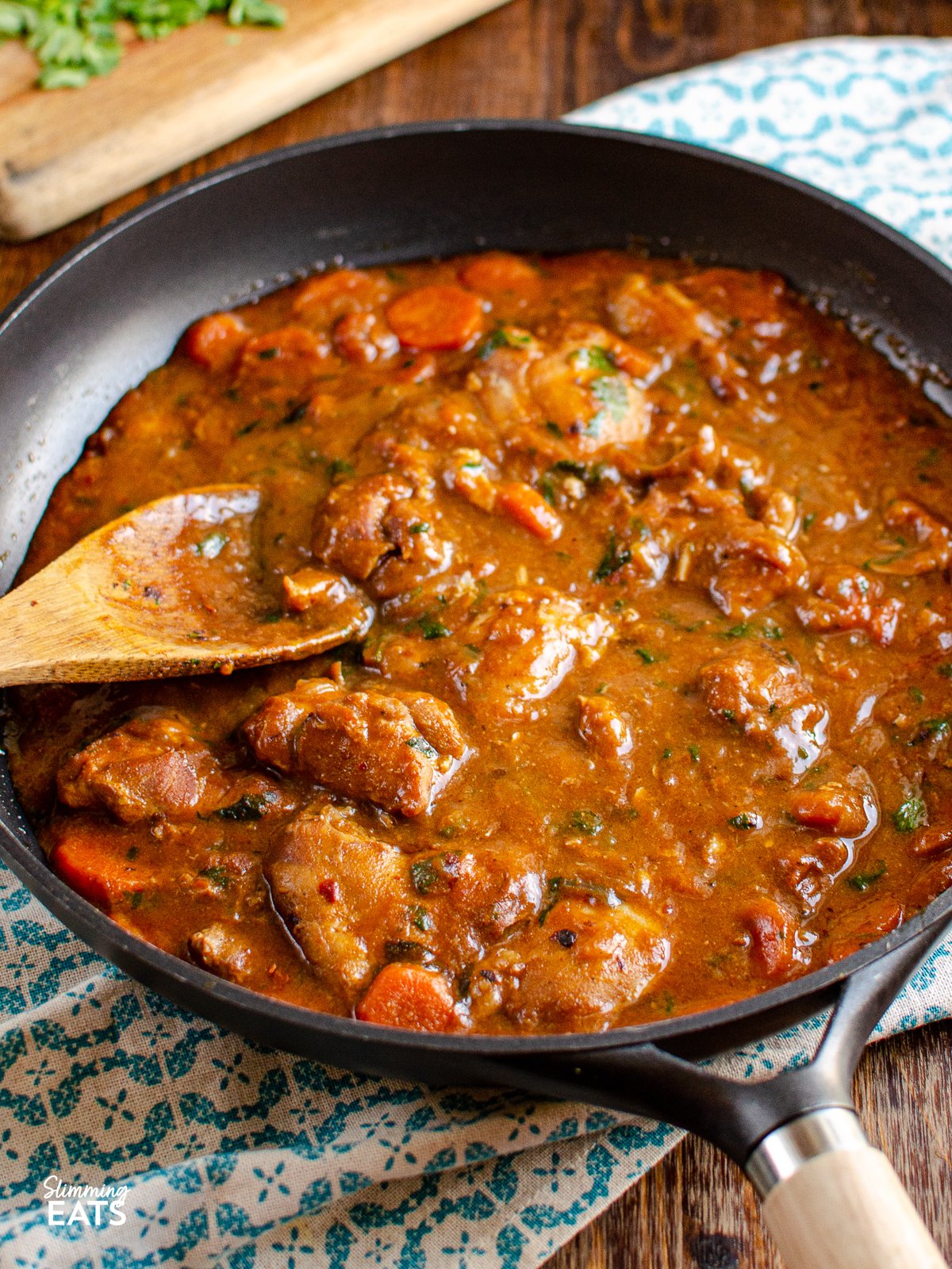 Homemade Sweet and Spicy Ginger Chicken in black frying pan with wooden spoon  