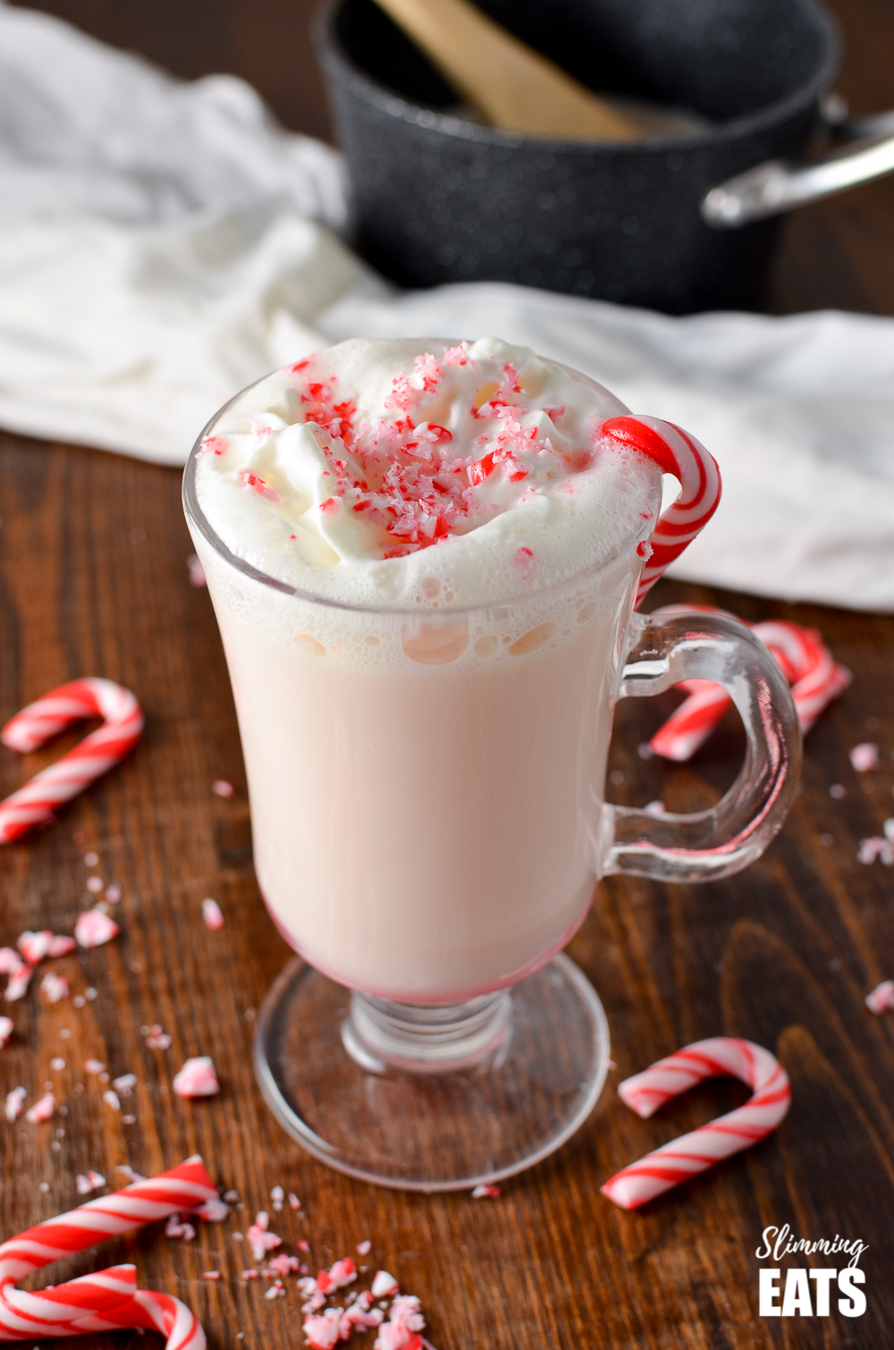 candy cane white hot chocolate in glass mug on wooden board with scattered broken candy cane pieces