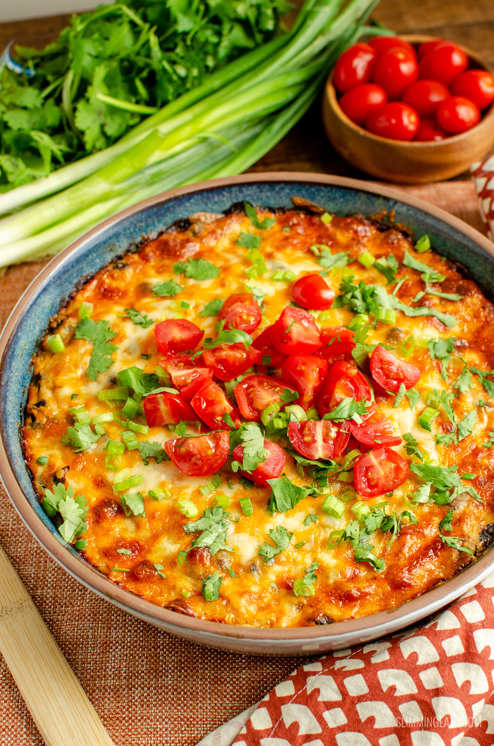 Mexican spaghetti squash bake in oven proof dish with green onions and tomatoes in background