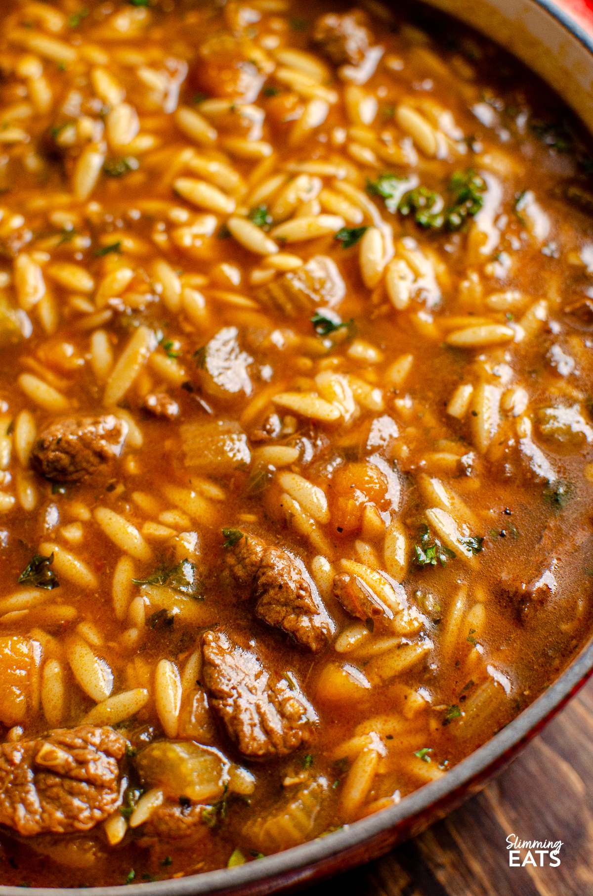 close up beef orzo stew in cerise cast iron pot with wooden spoon