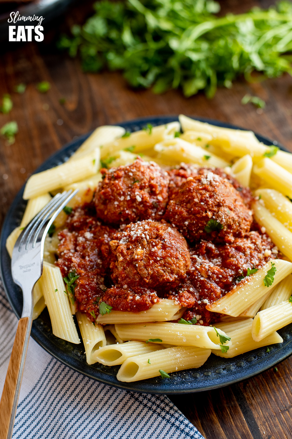 close up of slow cooker Italian chicken meatballs with pasta on navy plate with fork