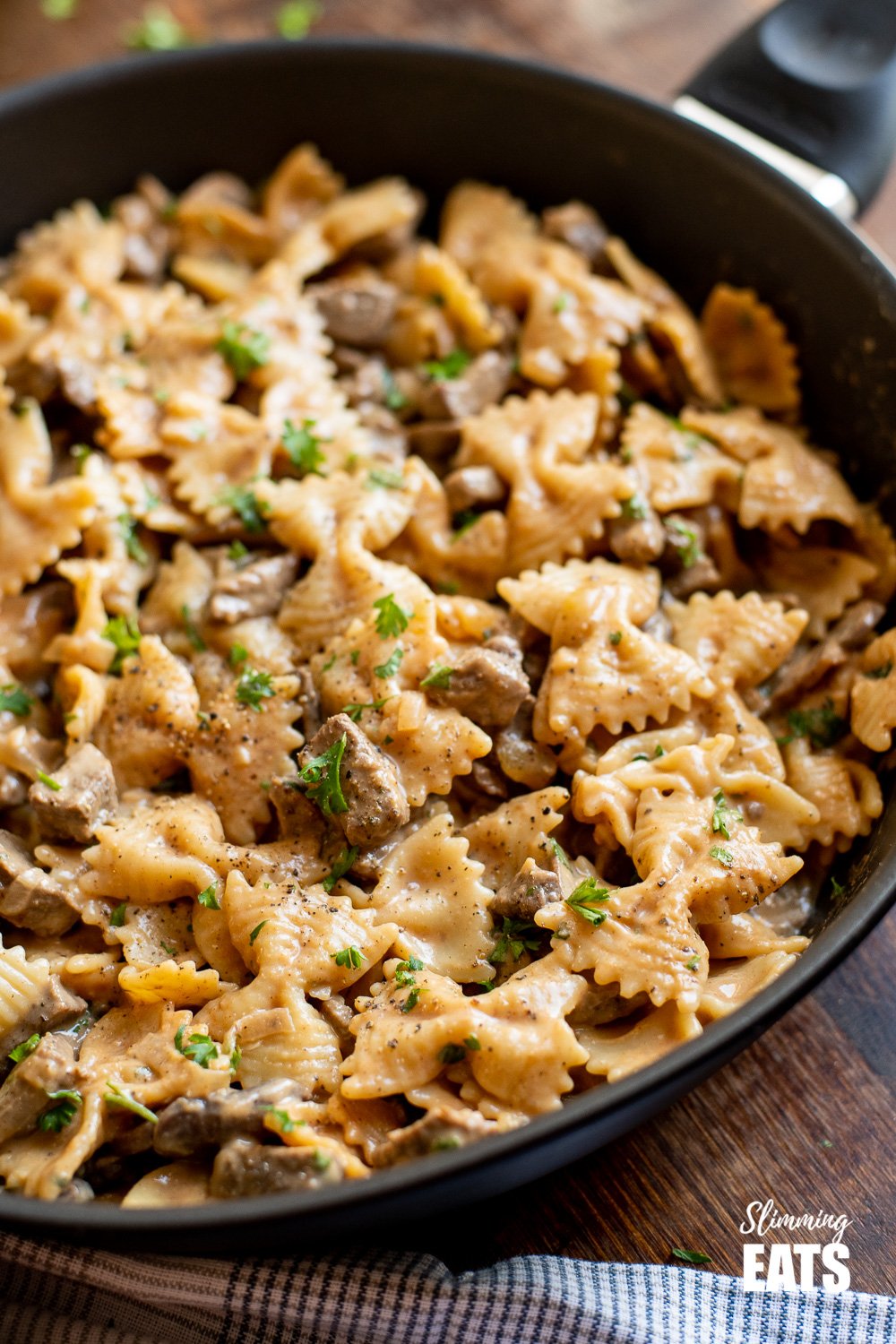 one pot beef stroganoff pasta in black frying pan on wooden board