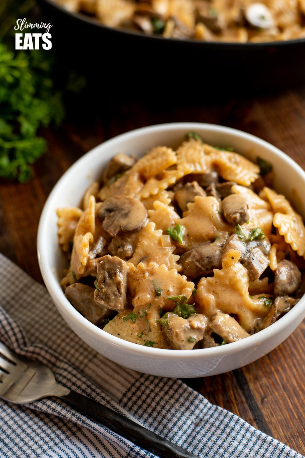 one pot beef stroganoff serving in white bowl with frying pan in background