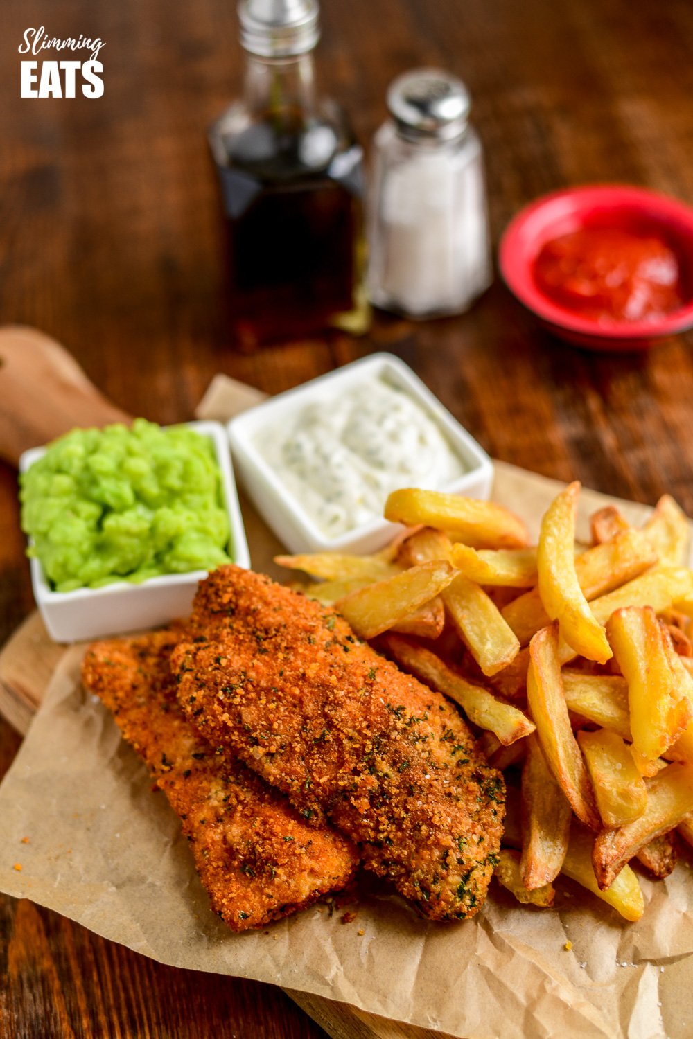 actifry fish and chips on crinkled parchment with mushy peas and tartare sauce in small white square dishes