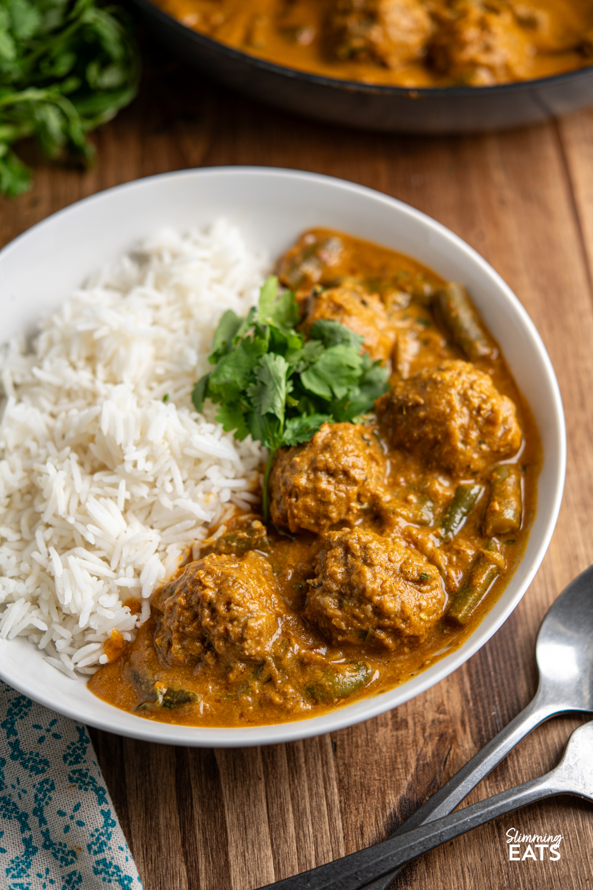 close up of coconut beef meatballs curry in white bowl with rice and coriander.