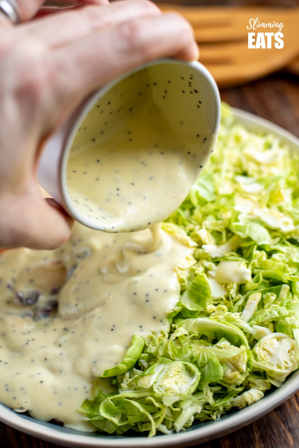 A delicious Healthy Brussels Sprouts Salad - with almond slices, crisp tart apple and sweet cranberries. Perfect on its own as a meal or as a side dish for your main Gluten Free, Vegetarian, Slimming and Weight Watchers friendly poppyseed dressing being poured on Brussels sprout salad in bowl