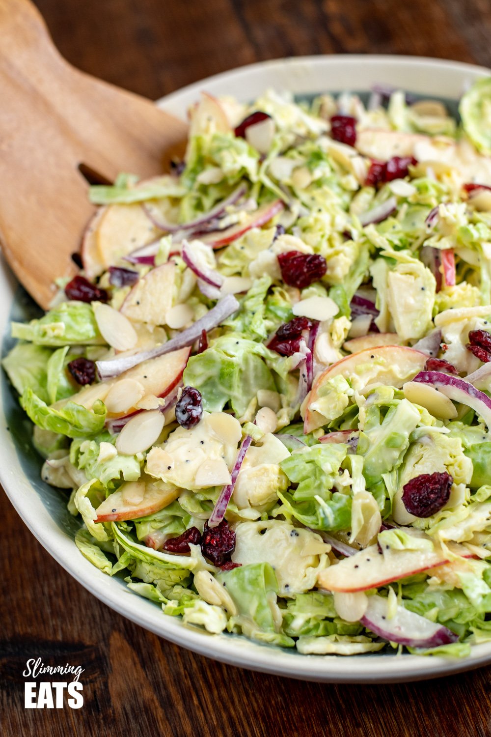 A delicious Healthy Brussels Sprouts Salad - with almond slices, crisp tart apple and sweet cranberries. Perfect on its own as a meal or as a side dish for your main Gluten Free, Vegetarian, Slimming and Weight Watchers friendly tossed brussels sprouts salad in bowl on wooden board