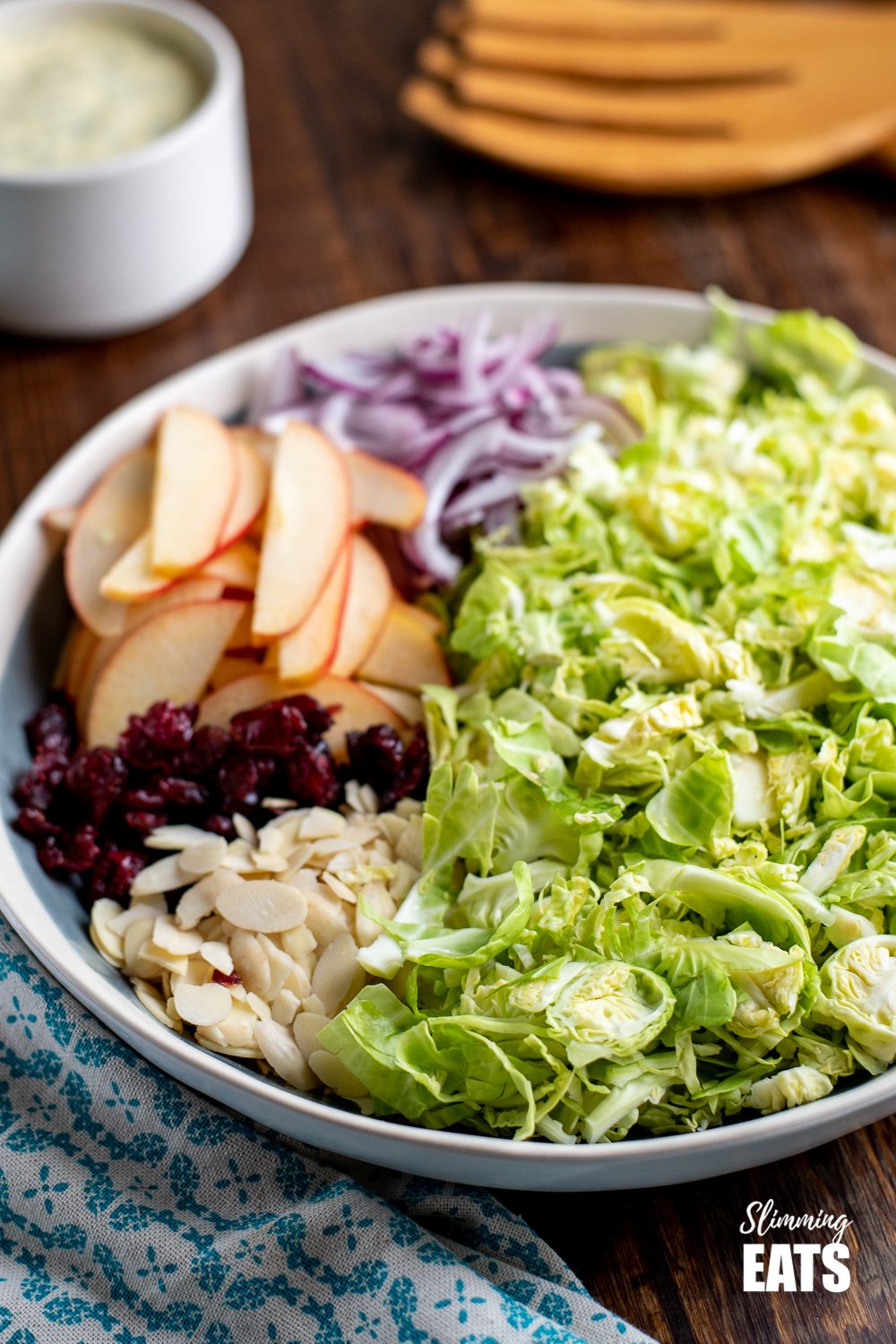 shredded brussels sprouts salad in a bowl with apples, red onion, cranberries and almonds on a wooden board