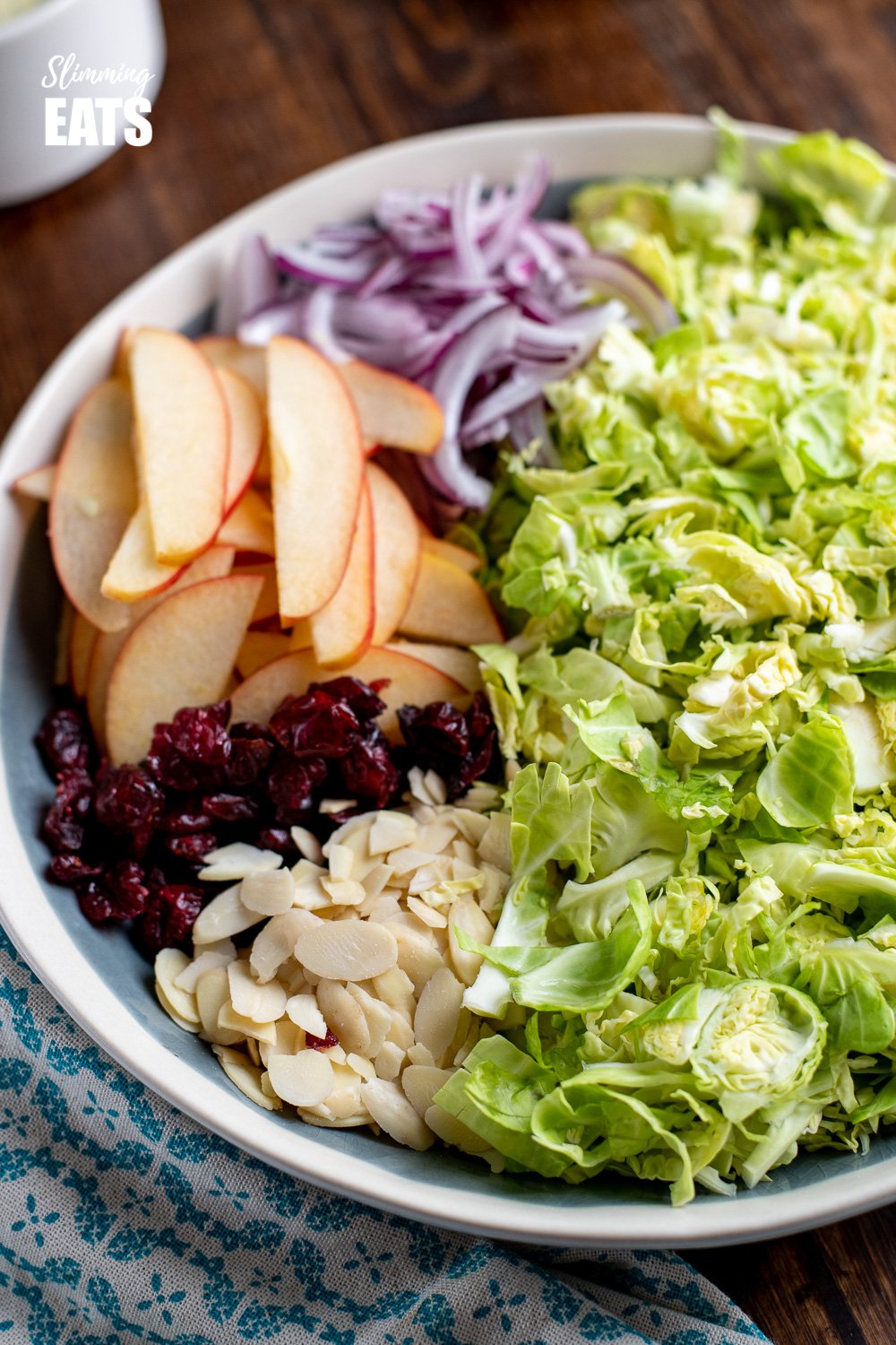 shredded brussels sprouts in a bowl with apples, red onion, almonds and cranberries