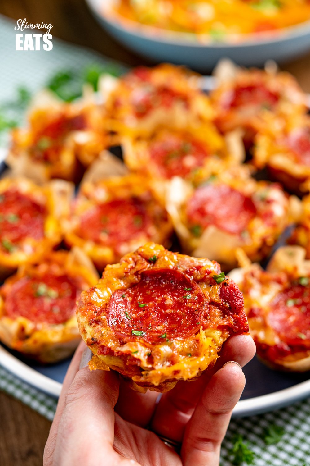 Drool-worthy Pepperoni Pizza Egg Bites - the mini cheesy bites are perfect for parties, tasters, lunches. Slimming and Weight Watchers friendly hand grabbing a Pepperoni Pizza Egg Bite from a blue plate