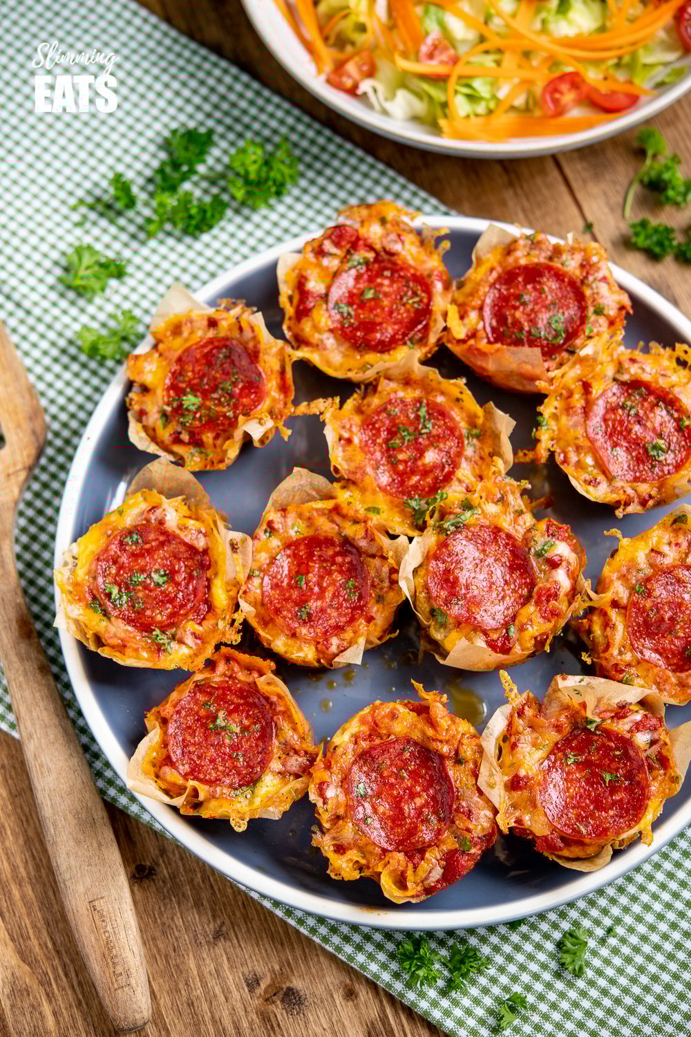 Drool-worthy Pepperoni Pizza Egg Bites - the mini cheesy bites are perfect for parties, tasters, lunches. Slimming and Weight Watchers friendly Pepperoni Pizza Egg Bites on a dark blue plate with a green checked tea towel
