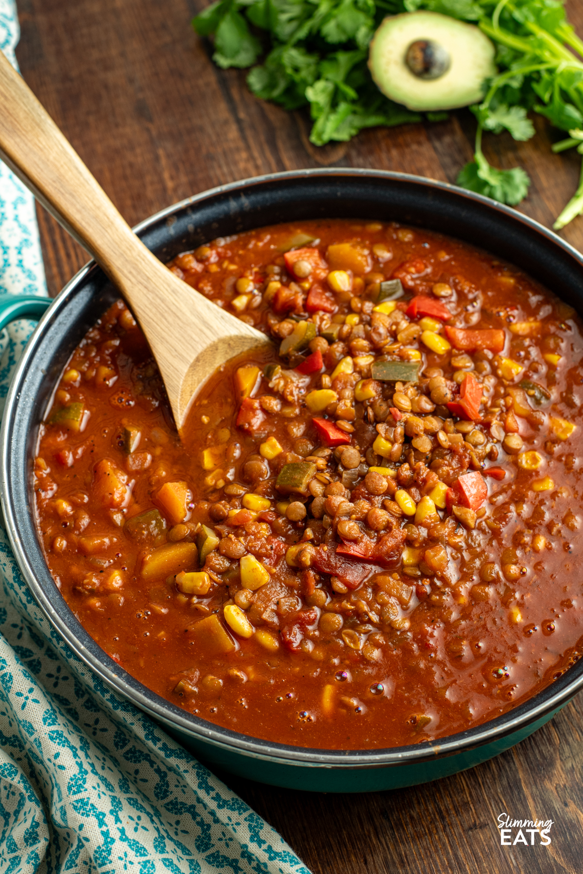 Taco Lentil Soup - the delicious spicy flavour of tacos using lentils instead of meat for a filling hearty meal that even the kids will enjoy. Gluten Free, Dairy Free, Vegan, Slimming and Weight Watchers friendly taco lentil soup in frying pan with wooden spoon on a wooden board with avocado and cilantro in background