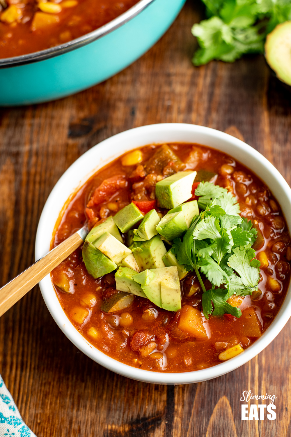 taco lentil soup in white bowl with wooden spoon topped with avocado and cilantro