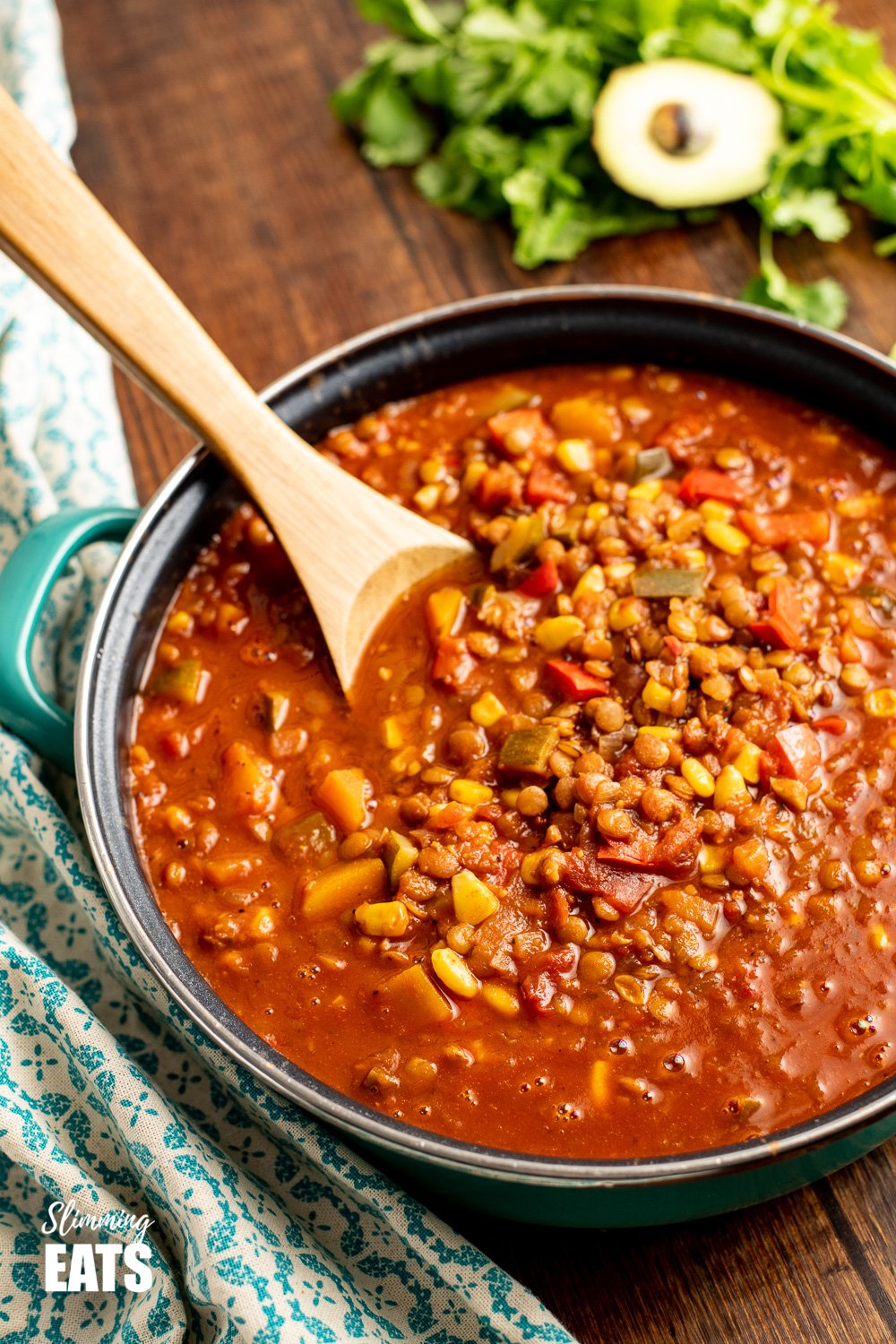 taco lentil soup in frying pan with wooden spoon on a wooden board with avocado and cilantro in background