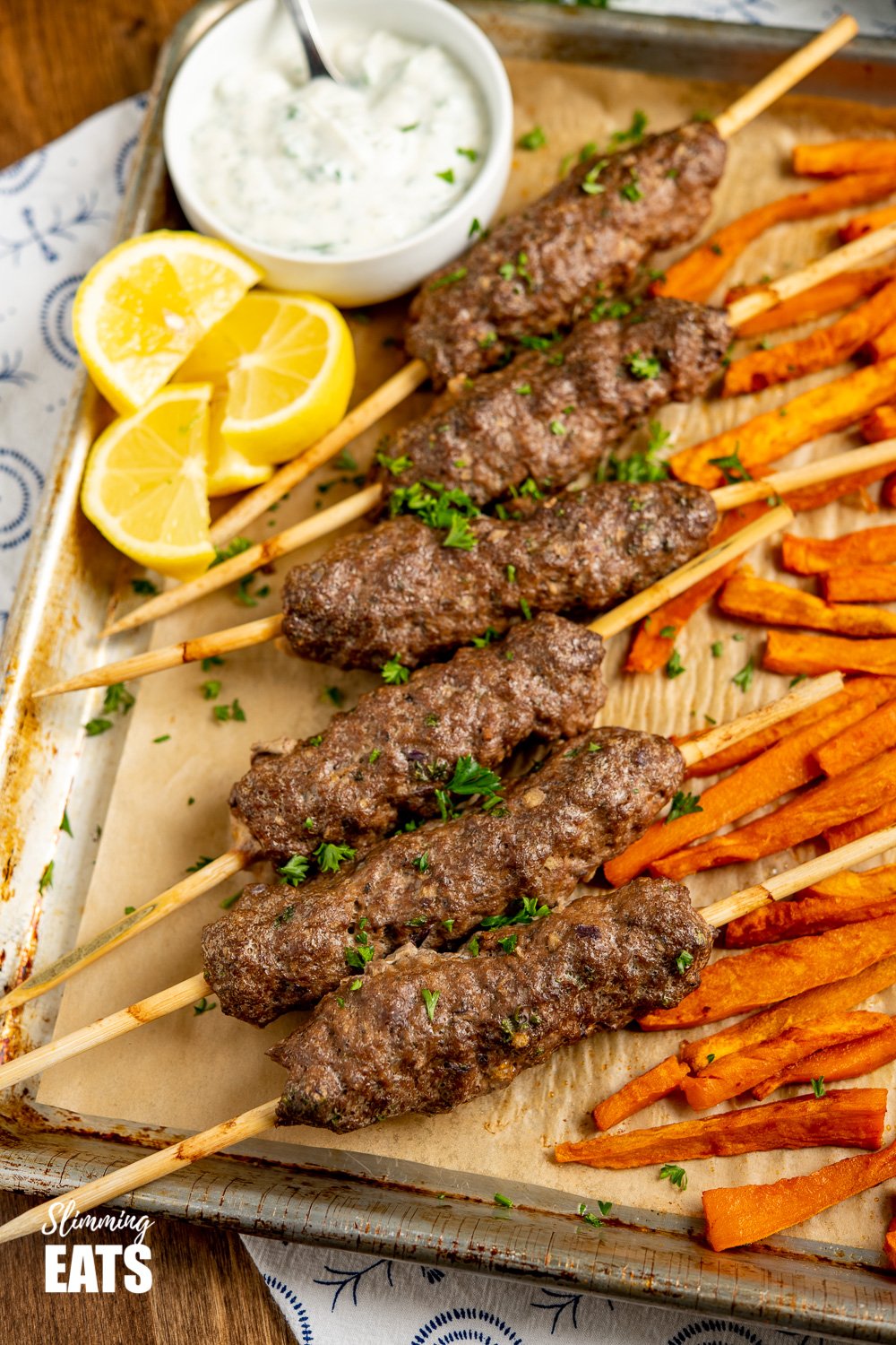 Yummy Beef Kofta Tray Bake - authentic Kofta kebabs with sweet potato fries and delicious roasted vegetables all finished off with a garlic yoghurt sauce. Gluten Free, Slimming Eats and Weight Watchers friendly Beef Kofta Tray Bake on baking tray with white bowl of garlic sauce and lemon slices