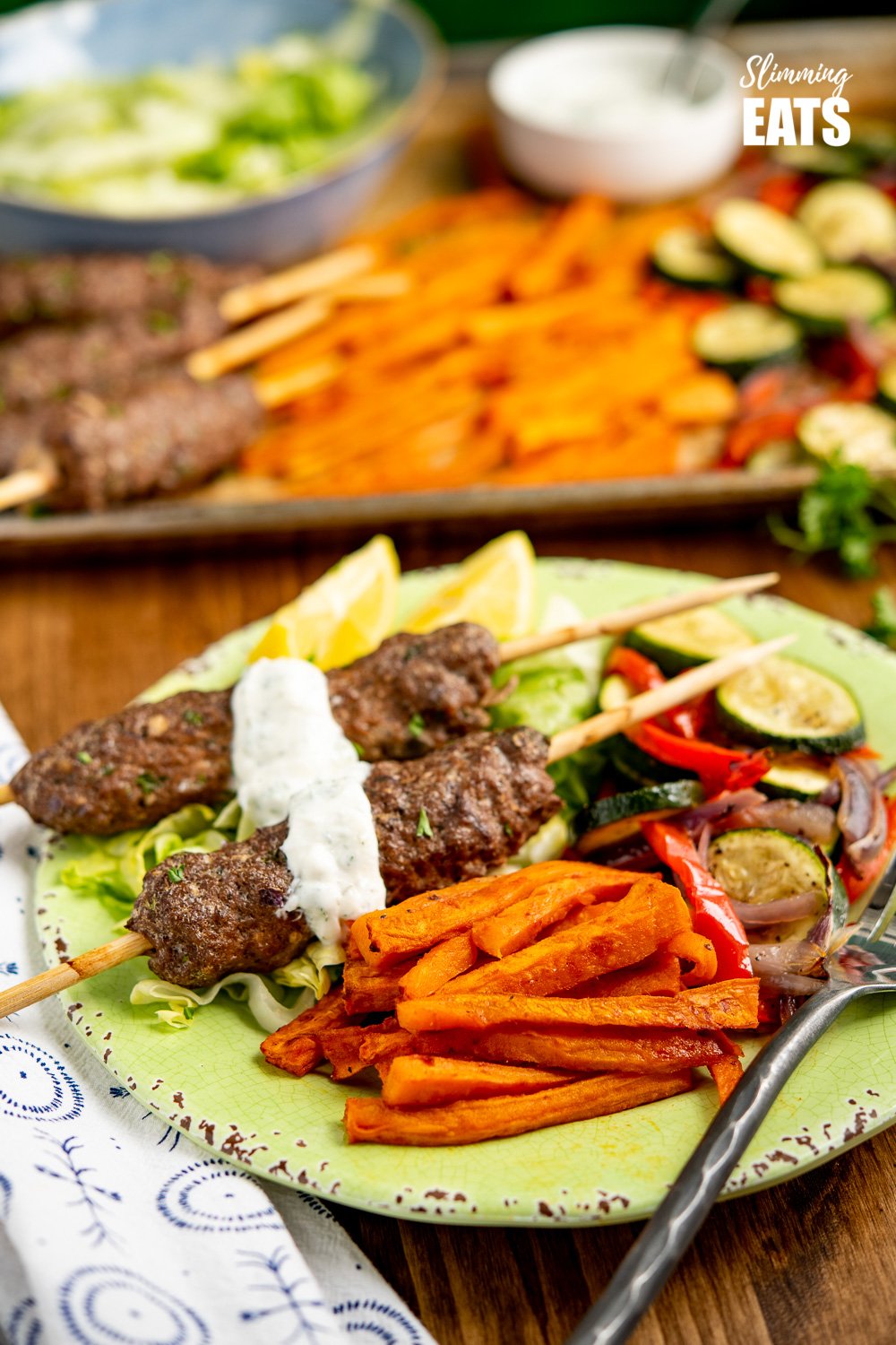Yummy Beef Kofta Tray Bake - authentic Kofta kebabs with sweet potato fries and delicious roasted vegetables all finished off with a garlic yoghurt sauce. Gluten Free, Slimming Eats and Weight Watchers friendly Beef Kofta Tray Bake served up on green plate with black handled fork and drizzle of garlic yoghurt sauce