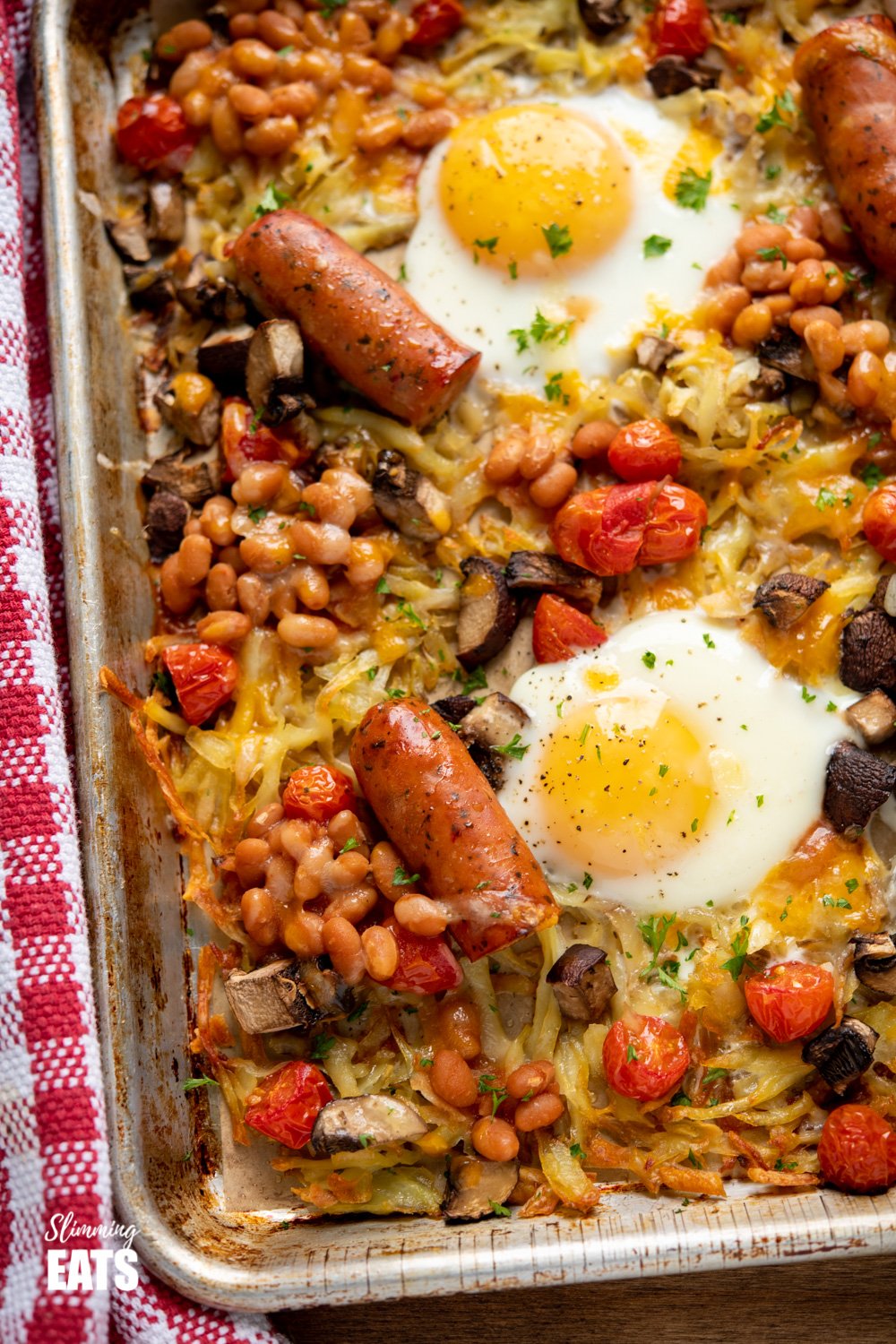 The Ultimate All Day Breakfast Tray Bake - so delicious, you will enjoy this easy simple recipe any time of day. Gluten Free, Vegetarian, Slimming Eats and Weight Watchers friendly close up of All Day Breakfast Tray Bake on a parchment lined baking tray with red checked tea towel to the side