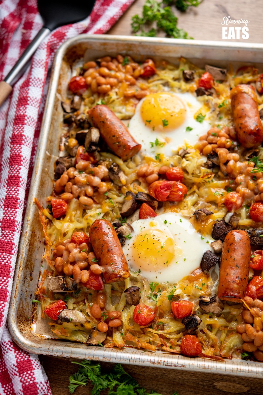 The Ultimate All Day Breakfast Tray Bake - so delicious, you will enjoy this easy simple recipe any time of day. Gluten Free, Vegetarian, Slimming Eats and Weight Watchers friendly All Day Breakfast Tray Bake on a parchment lined baking tray with red checked tea towel to the side