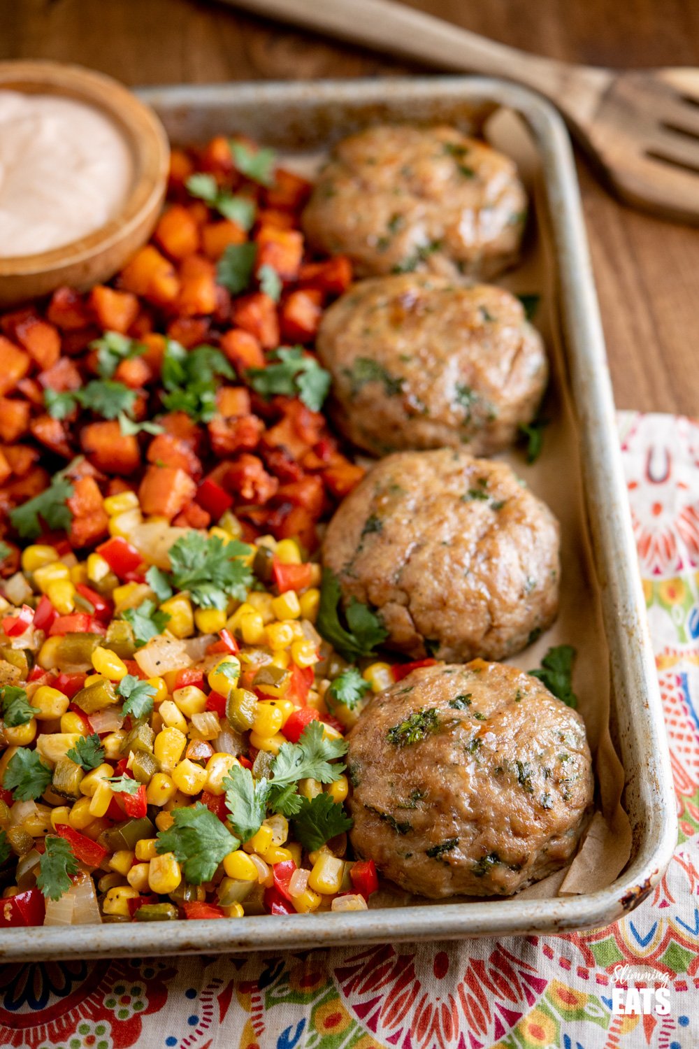 honey garlic chicken burgers on baking tray with roasted butternut squash, peppers and corn on wooden board.