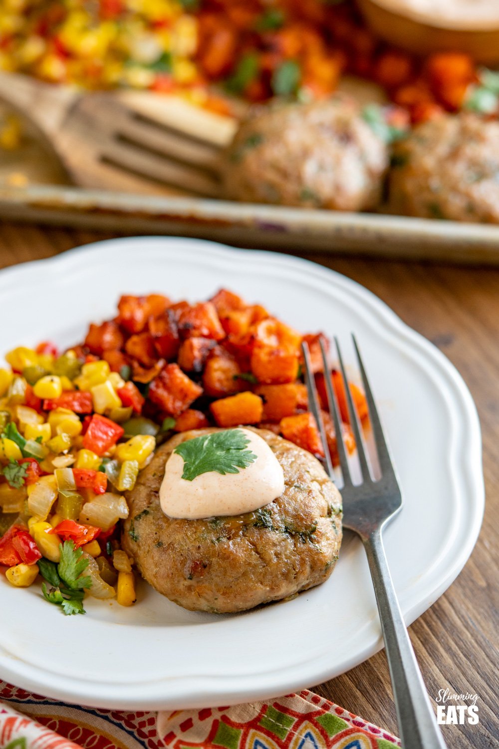 Honey Garlic Chicken Burger Tray Bake - tasty chicken burgers flavoured with honey and garlic all cooked on one tray with roasted butternut squash, peppers, onion and corn. Gluten Free, Slimming Eats and Weight Watchers friendly chicken burger topped with dip on white plate with silver fork
