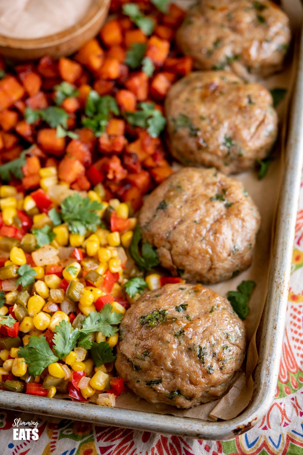 close up of burgers on baking tray with corn, peppers and butternut squash