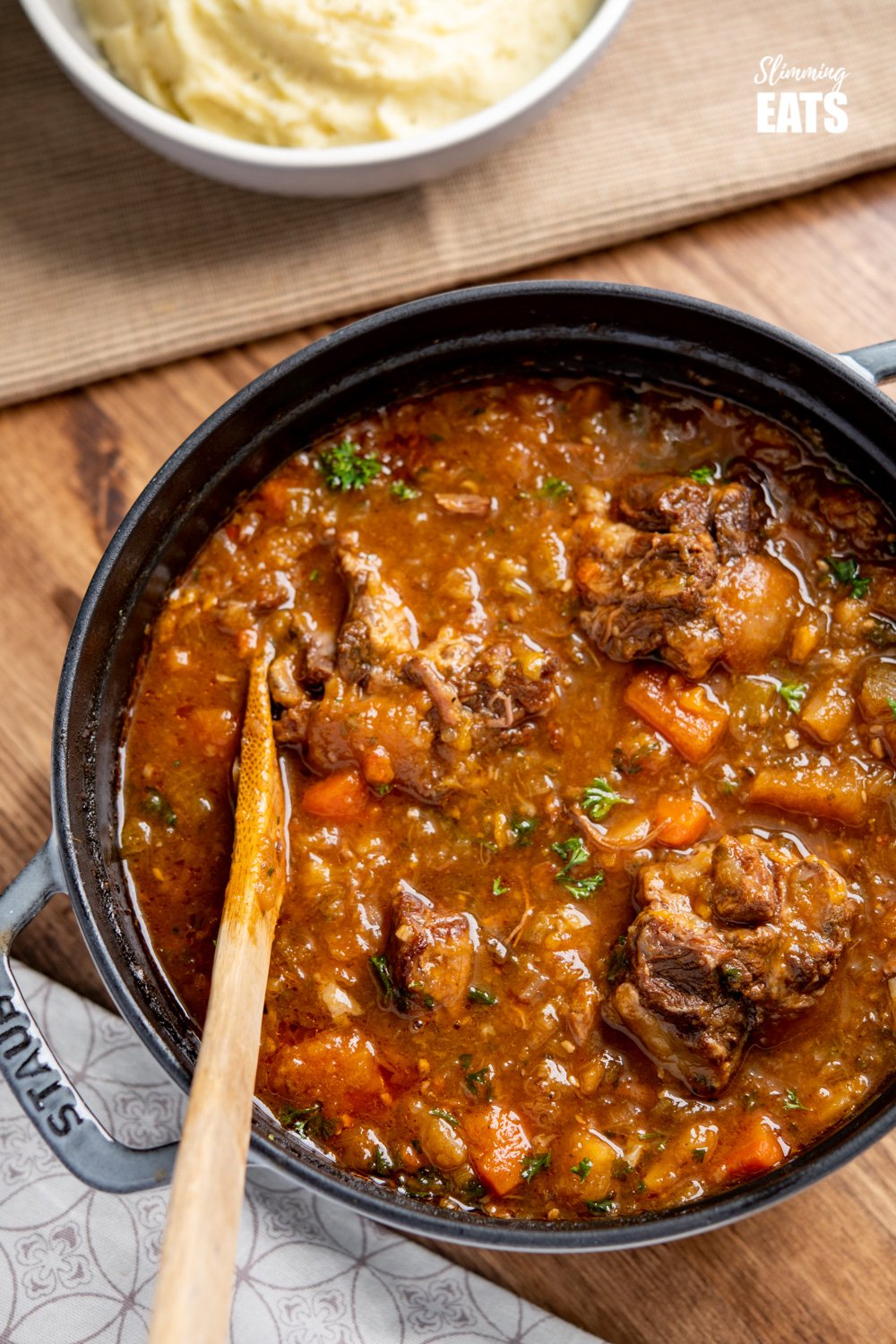 Hearty Oxtail Stew in a grey staub cast iron pot with wooden spoon