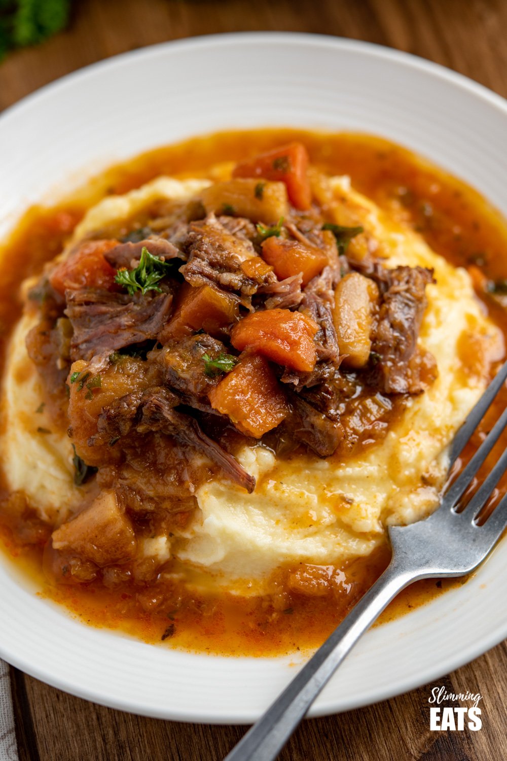 close up of Hearty Oxtail Stew over Syn Free mashed potatoes on white plate with silver fork