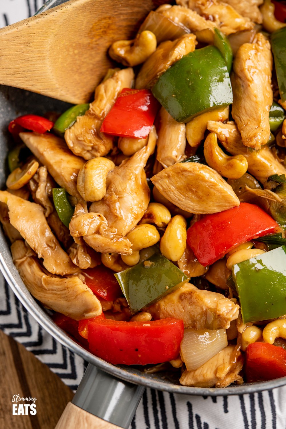 Chinese cashew chicken in a grey frying pan with wooden spoon