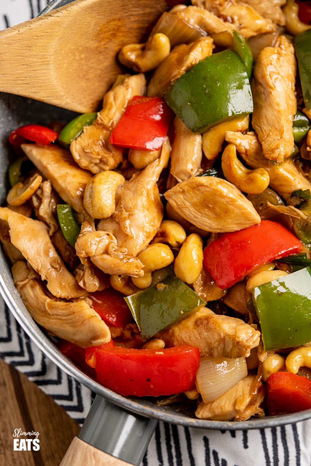 Chinese Cashew Chicken - amazingly tender pieces of chicken in a delicious sauce with cashew nuts and vegetables. Dairy Free, Slimming Eats and Weight Watchers friendly. Chinese cashew chicken in a grey frying pan with wooden spoon