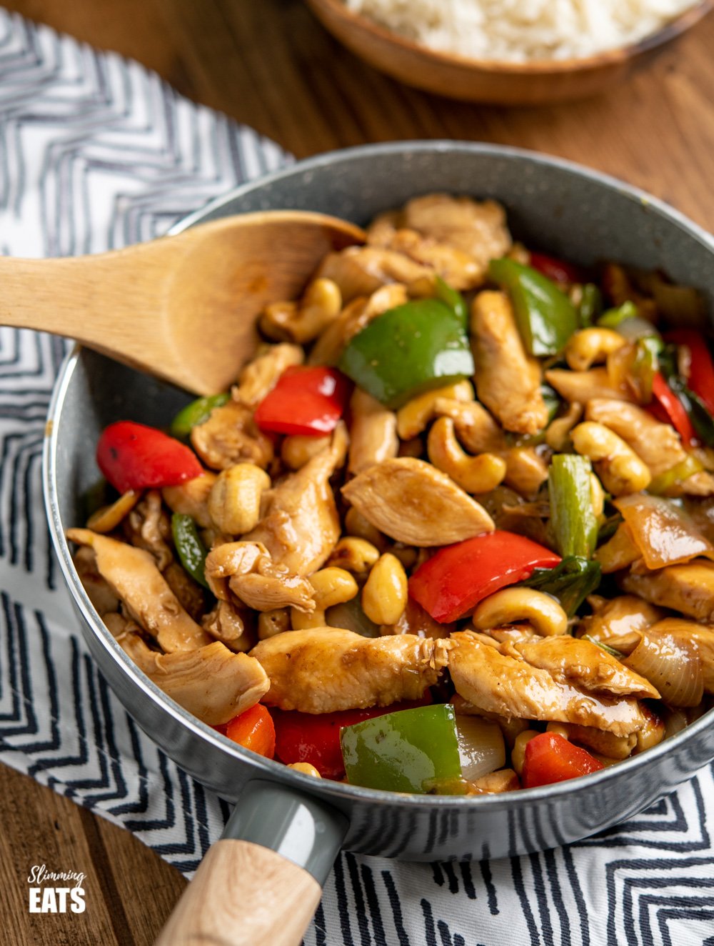 Chinese Cashew Chicken - amazingly tender pieces of chicken in a delicious sauce with cashew nuts and vegetables. Dairy Free, Slimming Eats and Weight Watchers friendly. Chinese Cashew Chicken in grey frying pan with wooden spoon