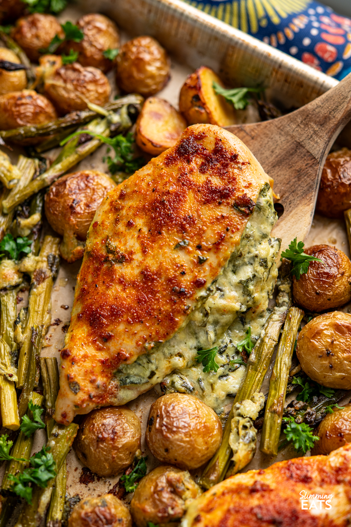 Creamy Cheesy Spinach Stuffed Chicken Tray Bake - Tender Juicy Chicken Breasts with a Creamy Parmesan Spinach Stuffing all baked on one tray with Baby Yukon Gold Potatoes and Asparagus. Gluten-Free, Slimming Eats and Weight Watchers friendly spatula lifting Creamy Cheesy Spinach Stuffed Chicken from baking tray