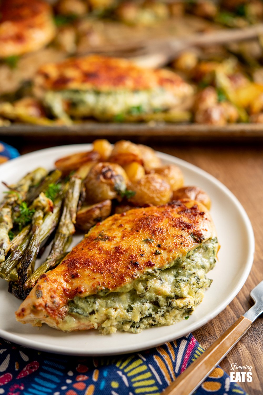 Creamy Cheesy Spinach Stuffed Chicken Tray Bake - Tender Juicy Chicken Breasts with a Creamy Parmesan Spinach Stuffing all baked on one tray with Baby Yukon Gold Potatoes and Asparagus. Gluten-Free, Slimming World and Weight Watchers friendly Creamy Cheesy Spinach Stuffed Chicken on plate with asparagus and roasted baby potatoes