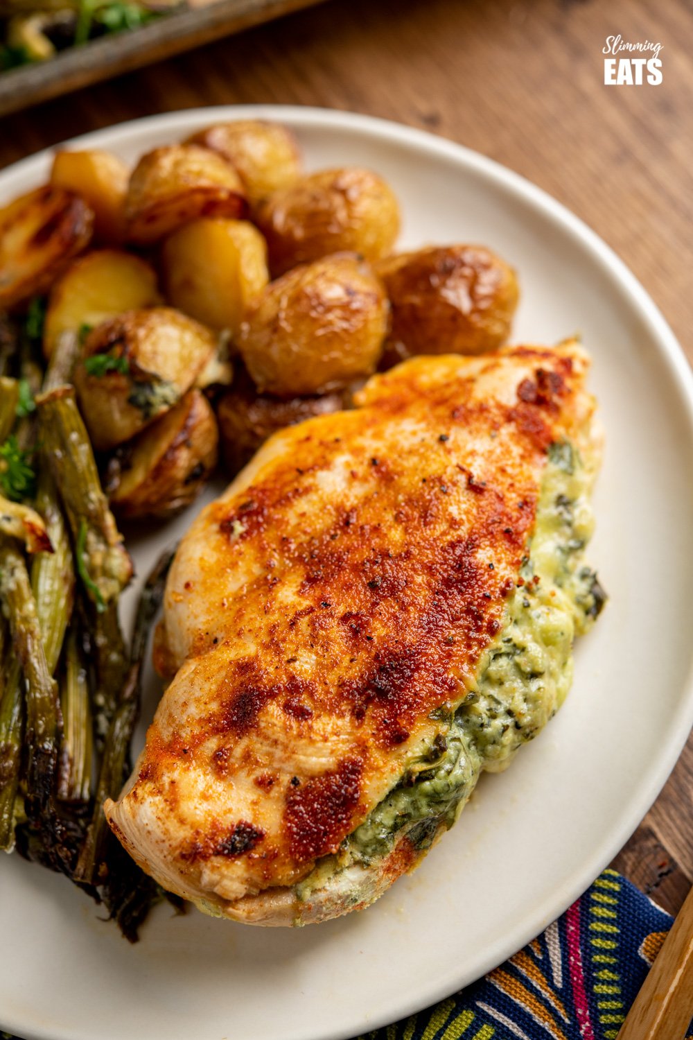 Creamy Cheesy Spinach Stuffed Chicken Tray Bake - Tender Juicy Chicken Breasts with a Creamy Parmesan Spinach Stuffing all baked on one tray with Baby Yukon Gold Potatoes and Asparagus. Gluten-Free, Slimming World and Weight Watchers friendly close up of Creamy Cheesy Spinach Stuffed Chicken on plate with asparagus and roasted baby potatoes