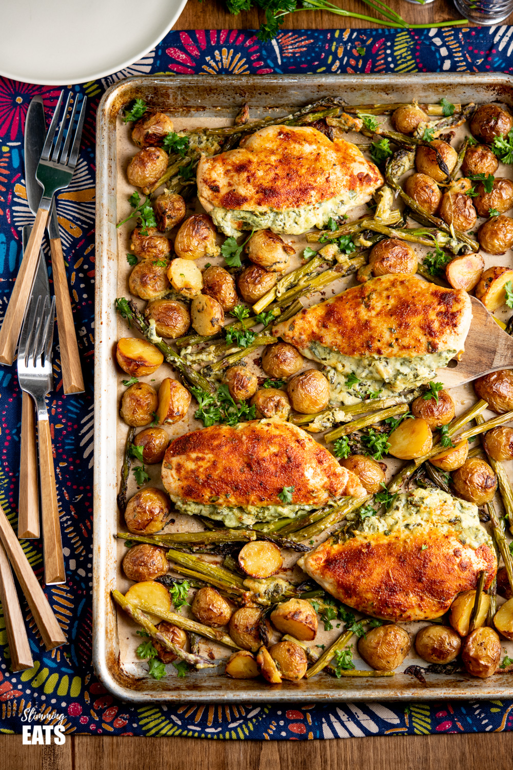 Creamy Cheesy Spinach Stuffed Chicken on a baking tray with roasted baby potatoes and asparagus