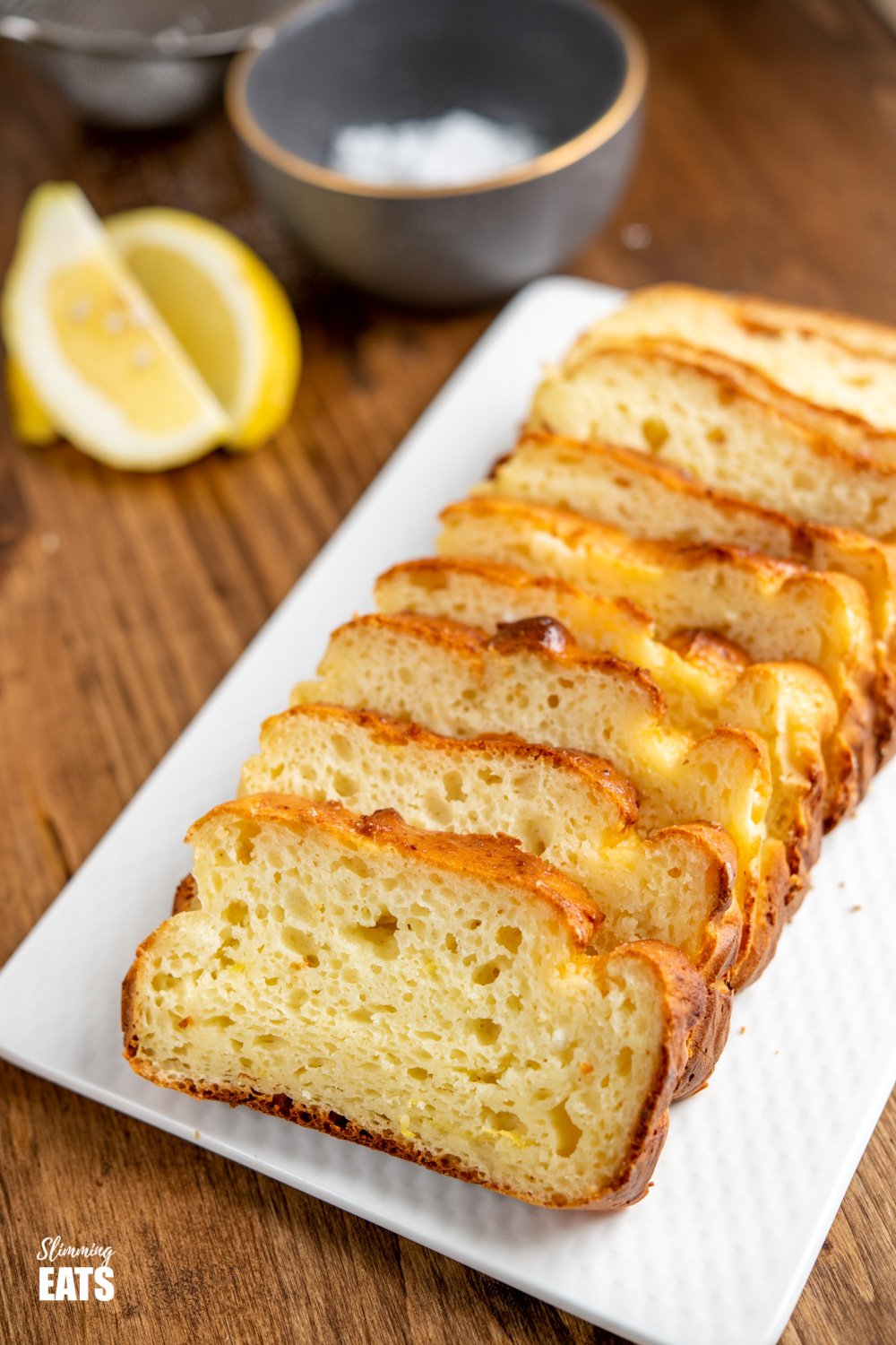 sliced lemon ricotta loaf on white plate with lemon slices in background