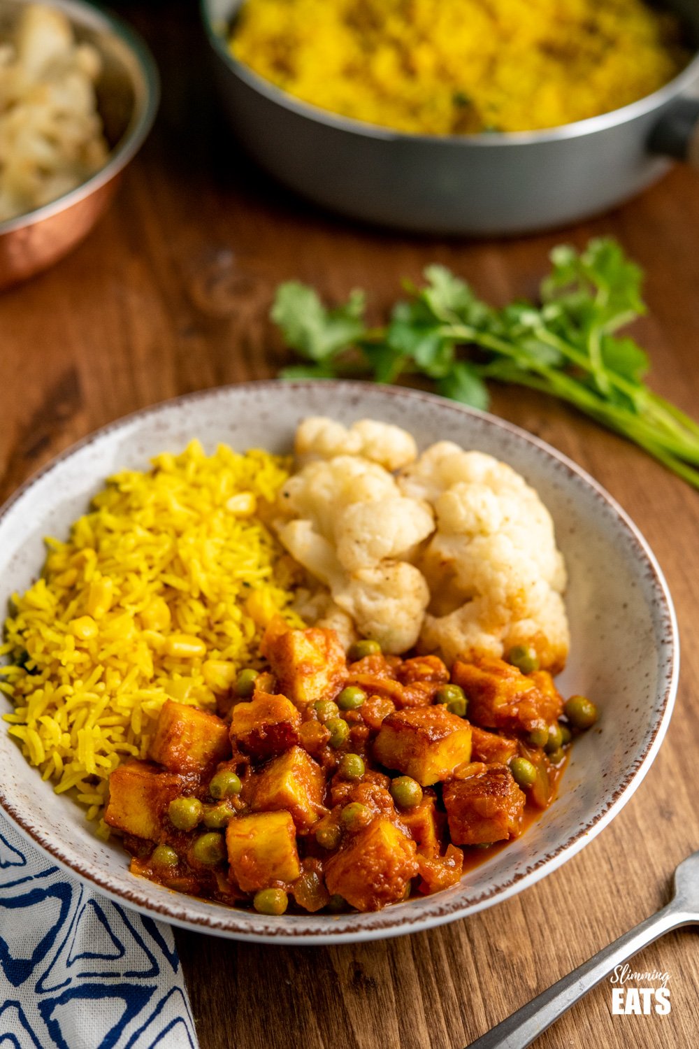 matar paneer curry in black frying pan in speckled bowl with roasted cauliflower and rice