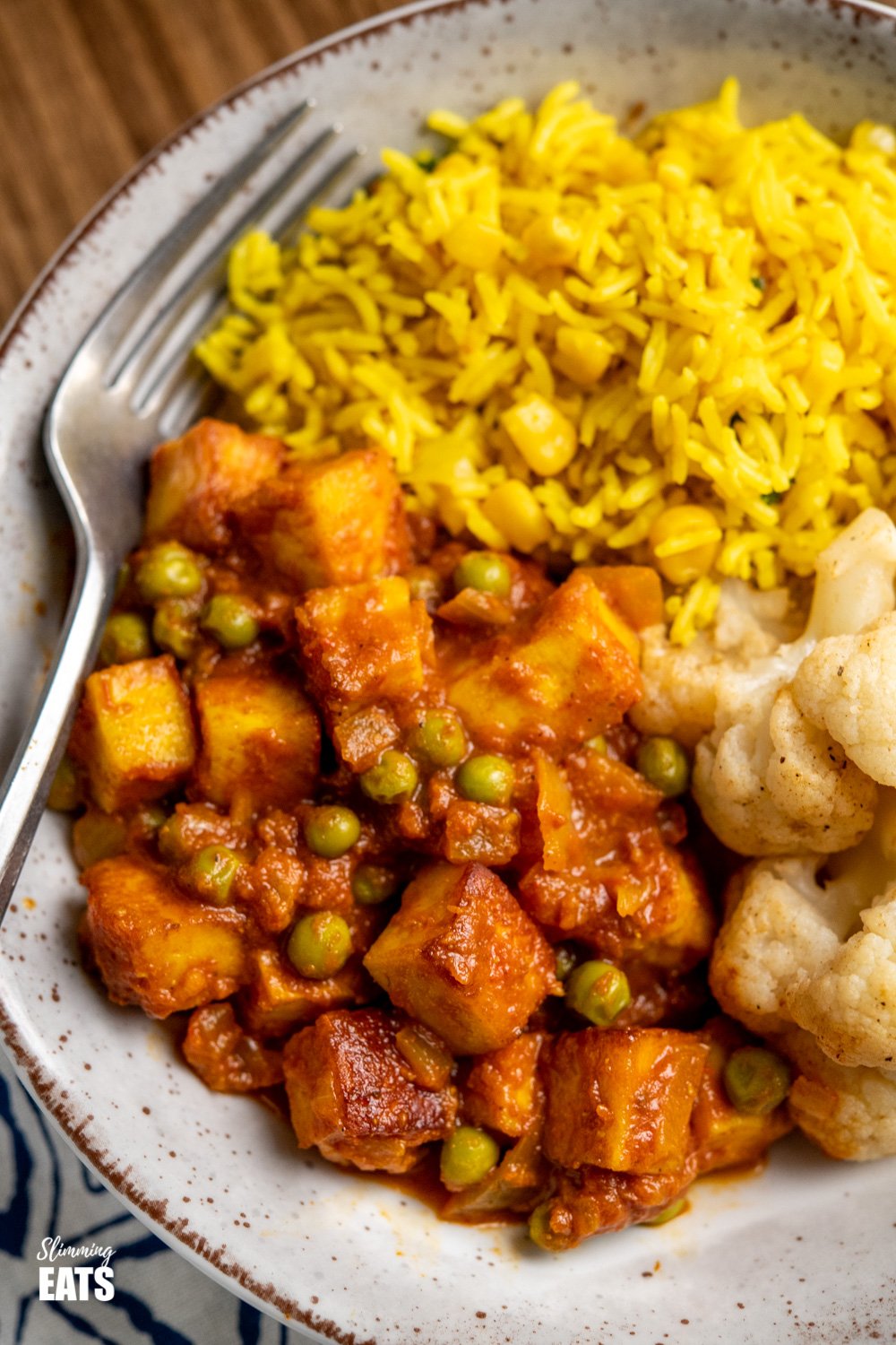 close up of matar paneer curry in black frying pan in speckled bowl with roasted cauliflower and rice