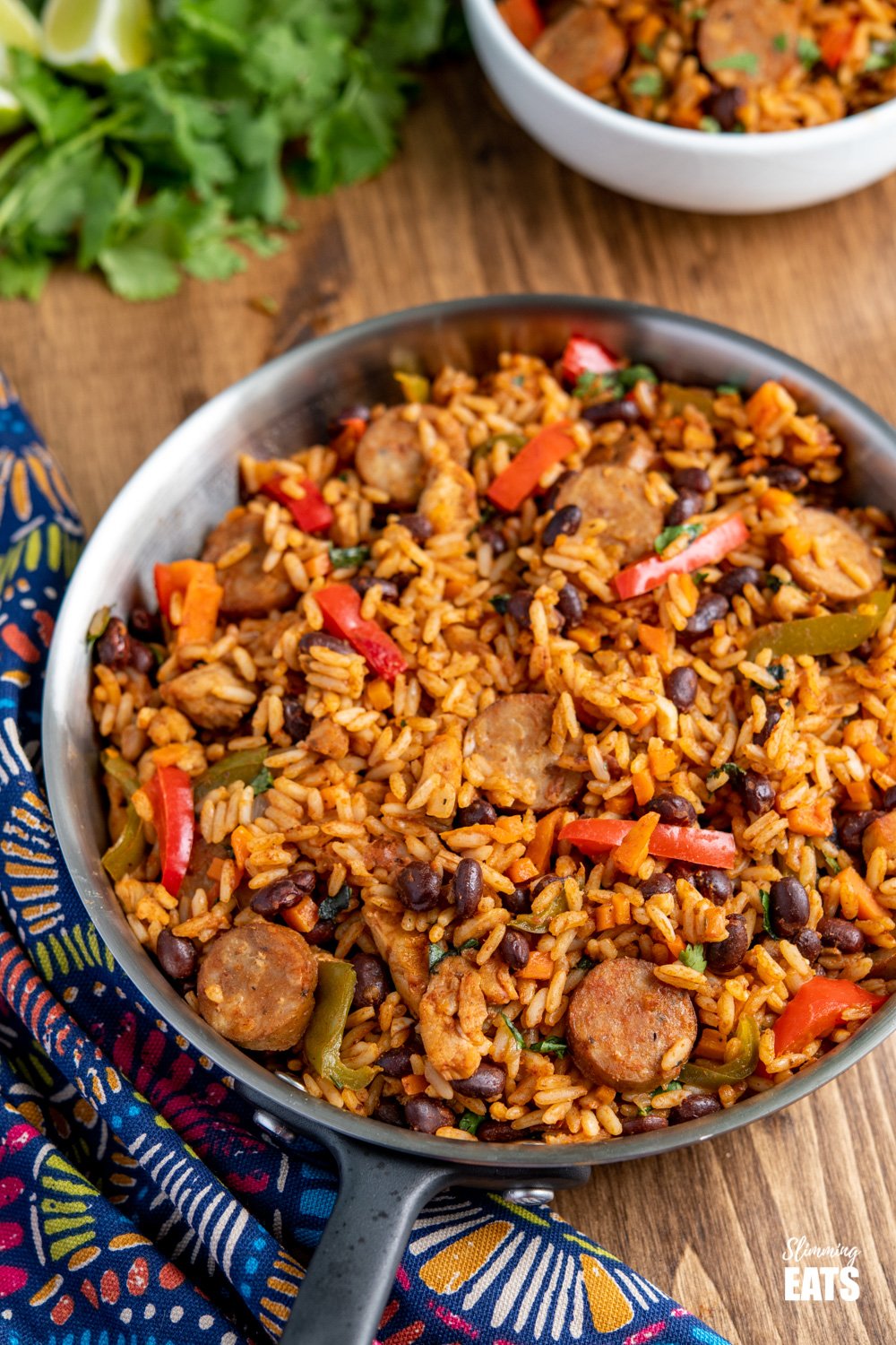 One Pot Cuban Style Rice (with Chicken and Sausage) - this delicious one-pot recipe with spicy seasonings, fresh vegetables and black beans is a perfect meal for any night of the week. Gluten Free, Dairy Free, Slimming Eats and Weight Watchers friendly One Pot Cuban Style Rice in frying pan with white filled bowl in background and cilantro and lime slices