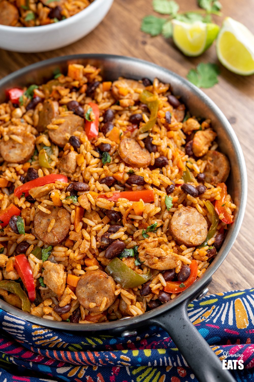 One Pot Cuban Style Rice in frying pan with white filled bowl in background and lime slices