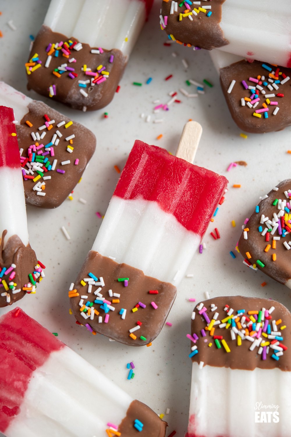 homemade fab ice lollies scattered on a white board surrounded by rainbow sprinkles