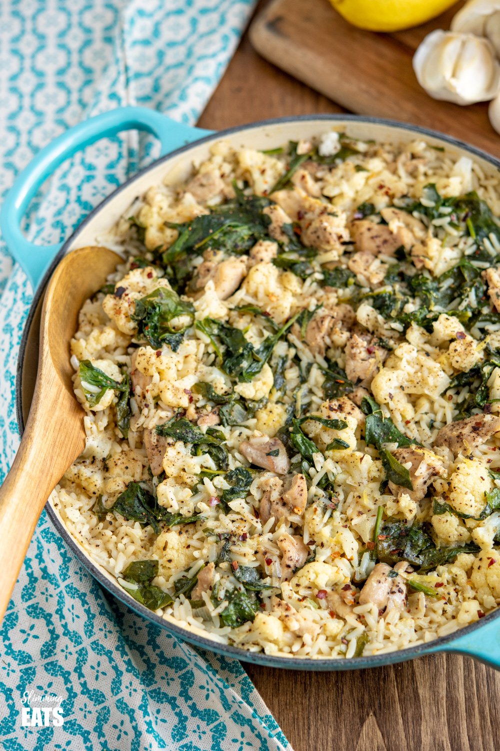 One Pot Lemon Garlic Chicken Rice - a simple all in one pan recipe with the delicious flavours of lemon and garlic and packed with healthy vegetables such as cauliflower and spinach. Dairy free, gluten free. one pot lemon garlic chicken rice in cast iron casserole pan with wooden spoon
